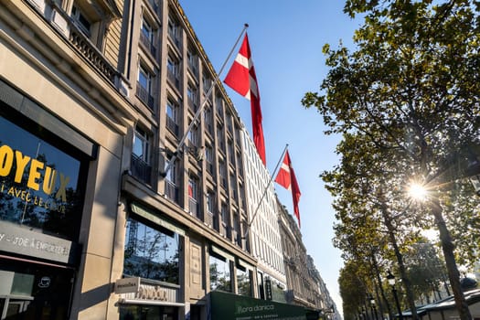 Central street of Paris The Avenue des Champs-Elysees with luxury shops and building with the Danish flag on it. Paris, France - November 24, 2024