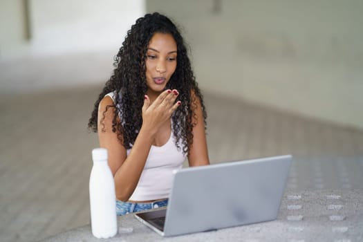A young woman with beautiful curly hair is engaged in an important video call on her laptop, focused and surrounded by a neat, minimalist background that enhances her modern workspace