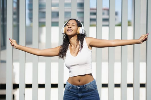 A carefree young woman dances joyfully outdoors in the sunshine, wearing stylish headphones and fully embracing the music, twirling with open arms, feeling the pure essence of freedom and fun