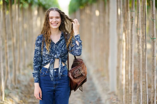 A joyful young woman stands gracefully among lush greenery, dressed in a stylish outfit and beaming with a radiant smile, embodying happiness and confidence for lifestyle and fashion themes