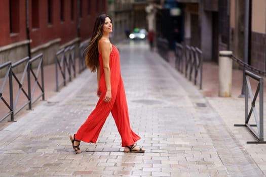 A confident woman in a vibrant red outfit walks gracefully down a serene street, embodying the union of fashion and natural beauty, captivating everyone with her cheerful demeanor