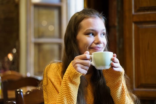 A young woman savors a warm cup of tea or coffee in a charming caf, radiating joy and relaxation
