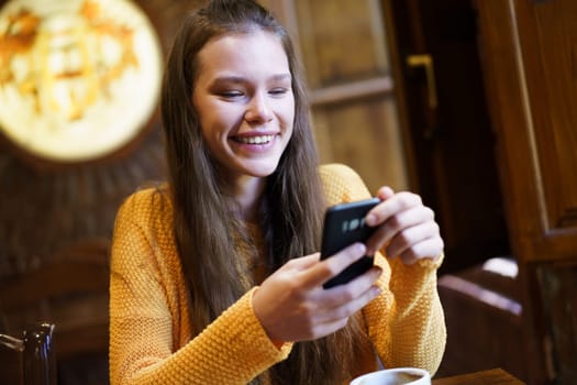 A young woman in a cozy caf smiles while texting on her smartphone. Warm lighting enhances the inviting atmosphere, perfect for social interactions
