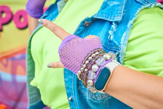 a woman's hand in a mesh glove with bracelets and watches. He was wearing a denim vest and a T-shirt. Fun 1990. Neon bright colors. disco.