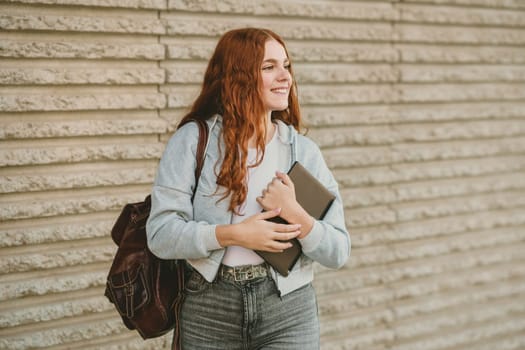 A vibrant young woman with long curly hair holds a modern tablet, wearing a trendy backpack, in front of a colorful wall, creating an inspiring atmosphere of positivity and creativity