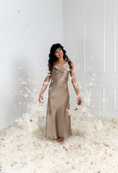 beautiful slender girl white feathers are flying around her. brunette girl with long hair. she is standing in a white room there are many white feathers around her. feathers are flying around her.