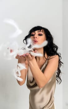 beautiful slender girl white feathers fly around her. brunette girl with long hair. in a bright room girl blows on feathers. fluff flutters around her, she is dressed in a beige silk dress.