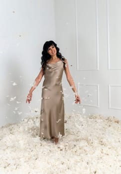 beautiful slender girl white feathers are flying around her. she is standing in a white room there are many white feathers around her. white feathers are flying in a bright room
