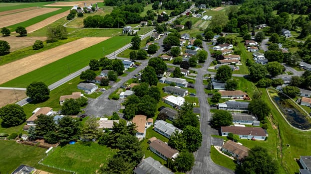 Aerial view of a tranquil rural community featuring various Mobile, Prefab, Manufactured houses situated near lush green fields and trees. The landscape shows harmonious blend of residences farmland.