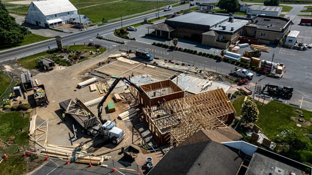 A construction project is progressing with workers actively framing a new building at a commercial location. The structure has wooden frames and is set amidst a clear sky and green landscape.