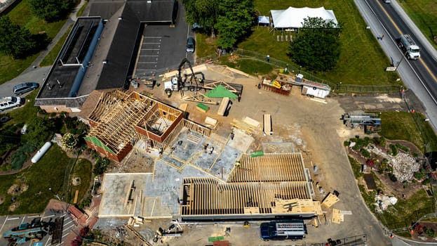 A construction project is progressing with workers actively framing a new building at a commercial location. The structure has wooden frames and is set amidst a clear sky and green landscape.