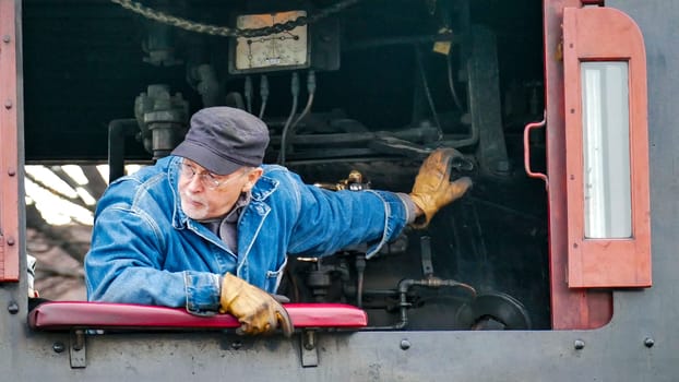 Strasburg, Pennsylvania, USA, December 31, 2024 - James Rice, A dedicated engineer adjusts the controls of a steam engine at a historic railway station, showcasing his expertise in maintaining vintage machinery on an autumn day.