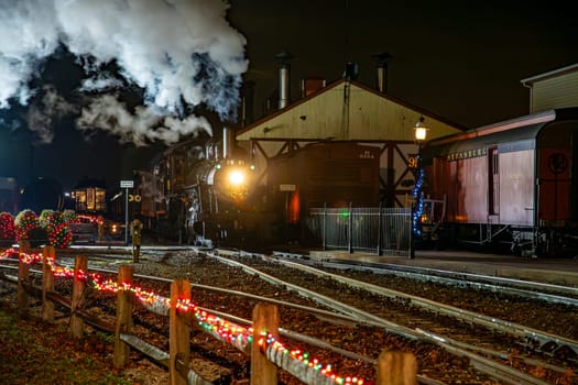 Strasburg, Pennsylvania, USA December 7, 2024 - A classic steam locomotive steams beside a festive station, adorned with colorful lights for the holiday season.