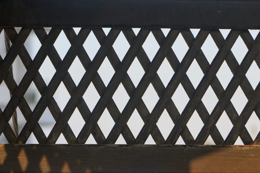 A wooden lattice casts captivating shadows in morning sunlight, showcasing its intricate craftsmanship.