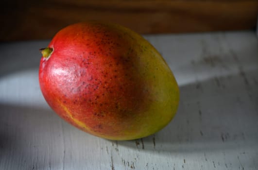 Ripe mango rests peacefully on a weathered wooden table, illuminated by golden afternoon sunlight.