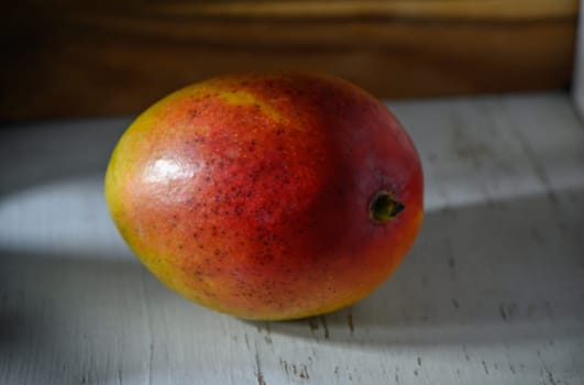 Brightly colored mango sits gracefully on a weathered wooden surface, showcasing its rich hues and inviting texture.