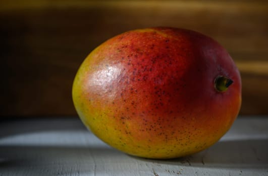 A vibrant mango showcasing its rich colors, resting against a warm wooden backdrop under gentle light.