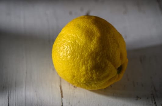 A vibrant lemon sits alone on a weathered table, basking in gentle light that highlights its textured skin.