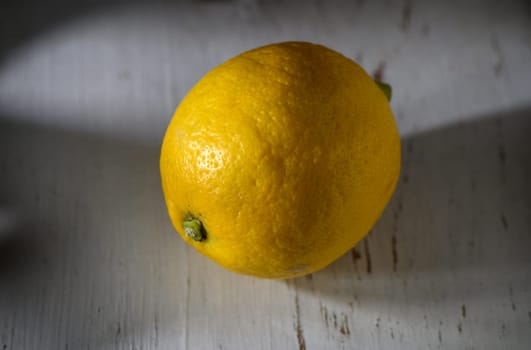 Golden lemon sits elegantly on weathered wood, showcasing its vibrant color and bumpy texture in gentle sunlight.