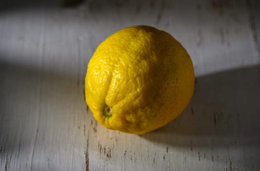 A vibrant lemon sits alone on a weathered table, illuminated by gentle sunlight, highlighting its texture.