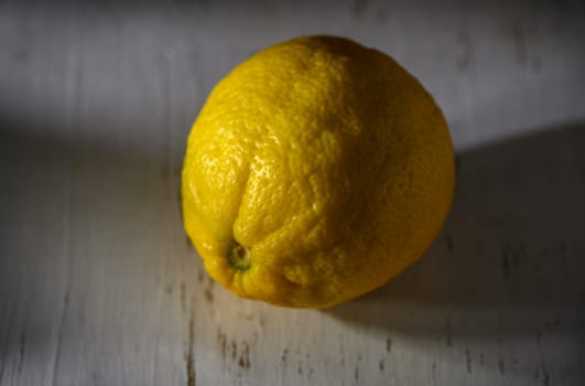 A vibrant lemon sits on a textured surface, exuding freshness and simplicity in the soft light of the day.