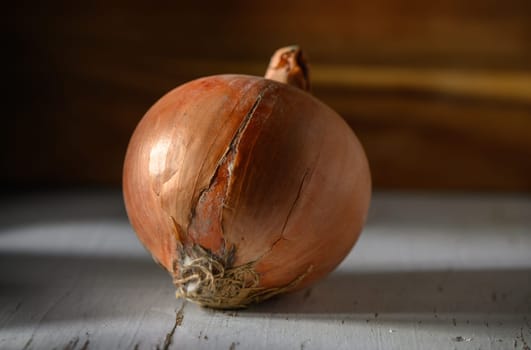 A rustic onion sits on a weathered wooden table, illuminated by warm, natural light, showcasing its unique texture.
