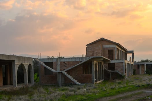 Ruins of an unfinished structure are bathed in warm light as dusk approaches, surrounded by wild grass and tranquility.