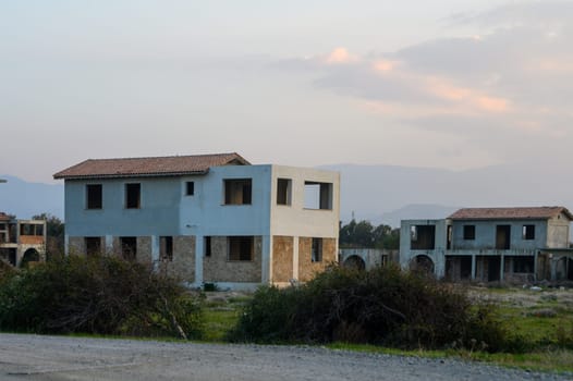 Abandoned structures emerge among overgrown weeds, bathed in the warm glow of twilight, evoking a sense of nostalgia.