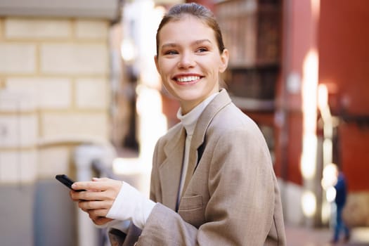 In a bustling city, a confident young woman in a chic outfit smiles while using her smartphone to connect with friends and strangers, showcasing her vibrant social life and modern style