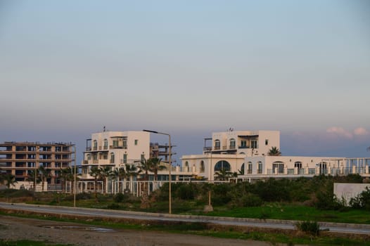Elegant white buildings stand surrounded by lush greenery and a calm sky as the day transitions to night.