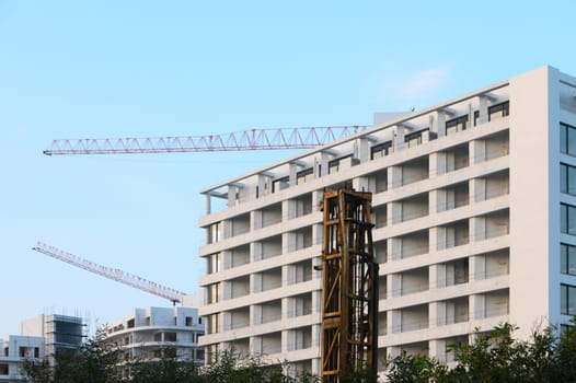 New residential structures rise with cranes overhead in a bustling cityscape under a bright blue sky.