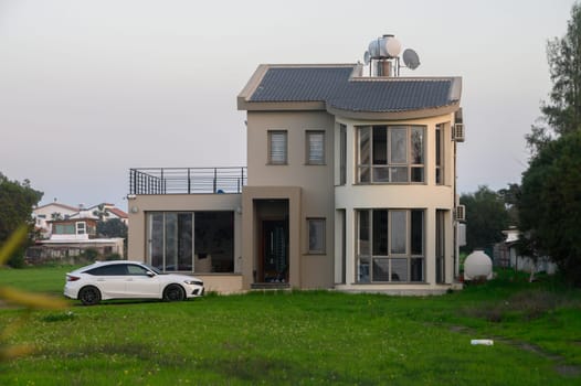 Stylish house stands prominently in lush surroundings, while a sleek white car adds elegance to the tranquil view.
