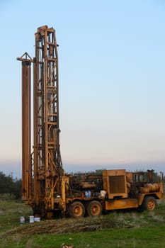 An old drilling rig operates quietly in a peaceful countryside, surrounded by green fields and early morning sunlight.