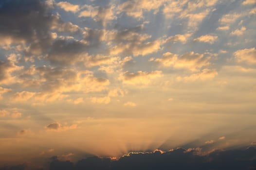 Brilliant hues of orange and gold fill the sky as sunlight streams through fluffy clouds during a serene evening.