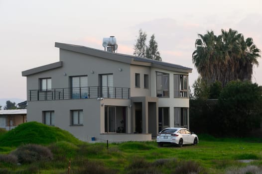 A sleek, contemporary house surrounded by verdant grass and palm trees during a serene twilight setting.