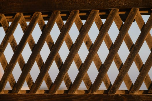 Golden hues illuminate intricate patterns of a wooden lattice during the tranquil evening hours.