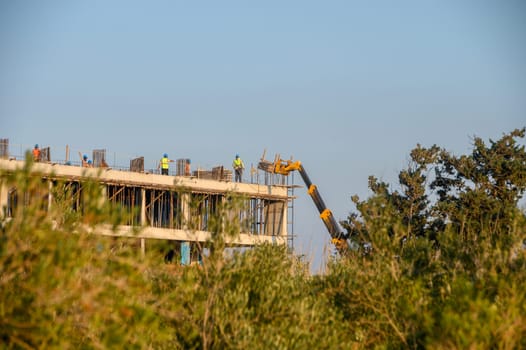Workers in safety gear are building a multi-story construct amidst greenery, showcasing teamwork and progress.