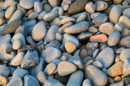 Smooth, colorful pebbles line the tranquil shoreline during a beautiful sunset, casting soft shadows on the sand.