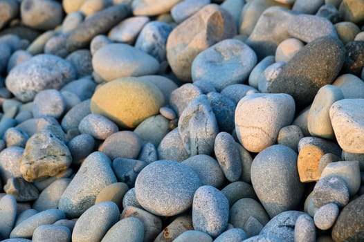 Smooth, colorful pebbles form a picturesque coastline, reflecting soft hues of a breathtaking sunset over the horizon.