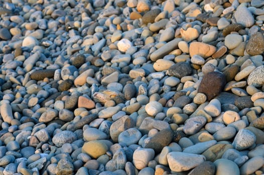 Smooth, multicolored stones blanket the riverbank, reflecting the gentle glow of dawn as water softly flows nearby.