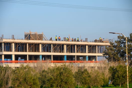 A group of construction workers is busy on a building site, creating a structure against a serene backdrop of trees.