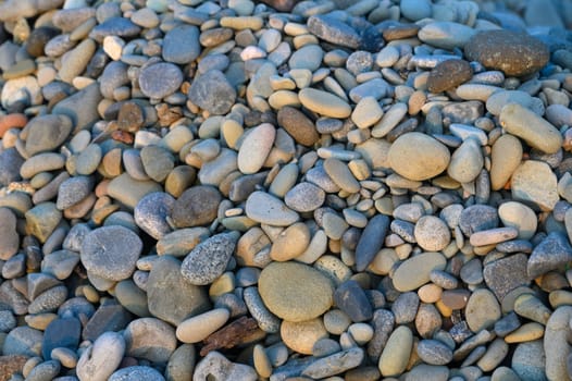 Smooth, colorful pebbles of various shapes and sizes create a serene riverside landscape under warm sunlight.