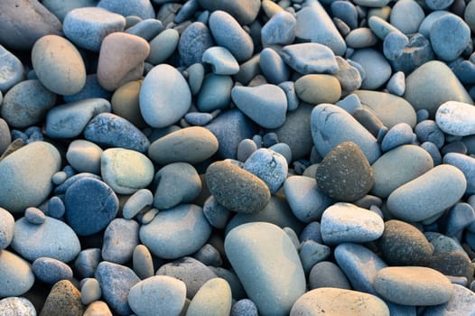 Smooth and vibrant pebbles blanket the shore, reflecting colors as the sun sets over the tranquil waters.