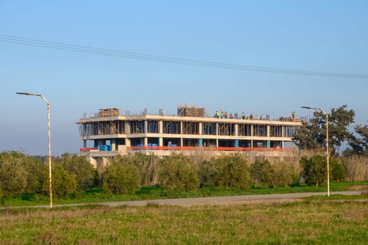 Workers are busy at a construction site for a new building surrounded by greenery and an open sky.