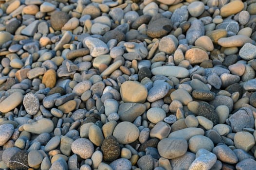 Smooth and varied pebbles blanket the beach at dusk, glistening softly under the fading sunlight’s warm glow.