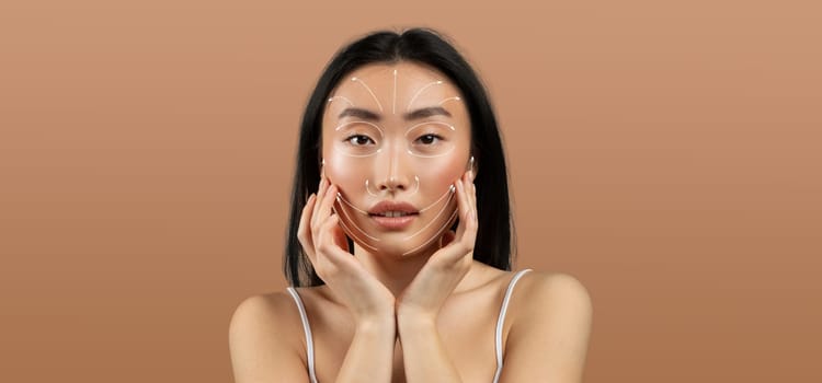 Asian woman practices her skincare routine, gently touching her face. She appears relaxed and focused, surrounded by an empty, neutral backdrop that emphasizes her beauty and self-care.