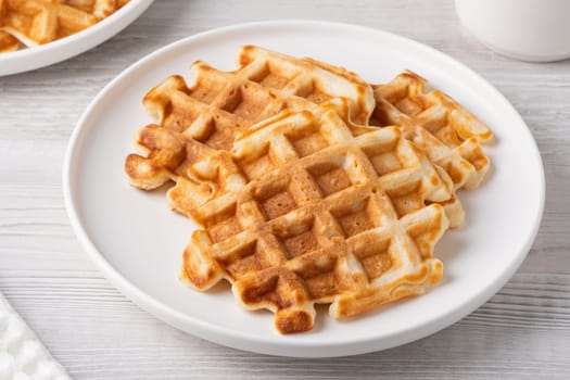Crispy golden waffles served on a round white plate in a cozy kitchen setting.