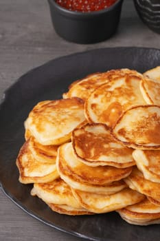 Delicious stack of golden pancakes served with cream and caviar on a rustic table.