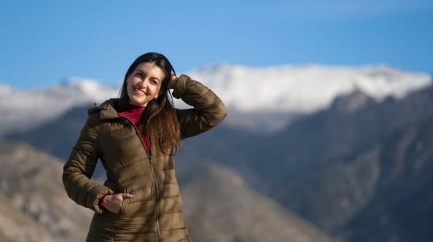 Happy tourist touching her hair while enjoying a beautiful snowy mountain view on a sunny winter day
