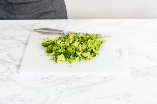 Chopping freshly steamed broccoli on a white cutting board.